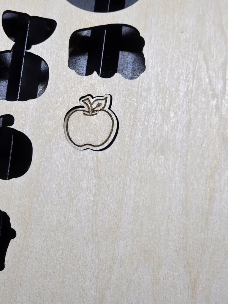 a laser earring design, shaped like an apple, still in the sheet of wood
